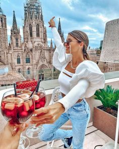 a woman in white shirt and jeans holding wine glasses with strawberries on the table