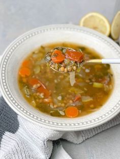 a spoon full of soup with carrots, beans and lemon wedges on the side