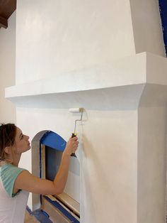 a woman is painting the wall with white paint