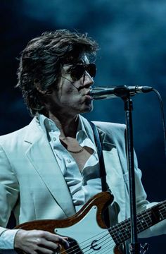 a man in white suit and sunglasses holding a guitar while standing next to a microphone