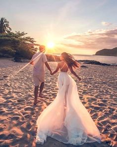 two people holding hands while walking on the beach at sunset, with the sun setting behind them