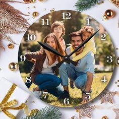 a clock with two people on it surrounded by christmas decorations and gold ornaments, including pine cones