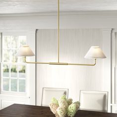 a dining room table with two lamps hanging from it's ceiling and flowers in the center