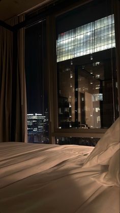 an unmade bed in front of a window with city lights on the windowsill