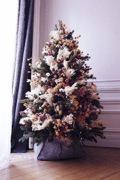 an artificial christmas tree in a pot on the floor next to a curtained window