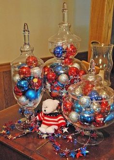 a table topped with glass vases filled with christmas balls and ornaments next to a teddy bear