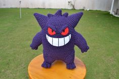 a purple crocheted stuffed animal sitting on top of a wooden table in the grass