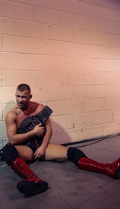 a shirtless man sitting on the floor with his legs crossed and wearing red boots