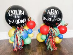 two black balloons with red, yellow and green streamers are on the floor next to each other