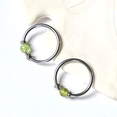 two silver hoop earrings with green beads on white cloth background, closeup view from above