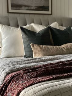 a bed with many pillows on top of it and a painting above the headboard