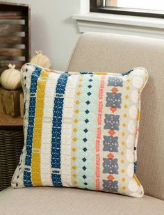 a pillow sitting on top of a couch next to a basket filled with pumpkins