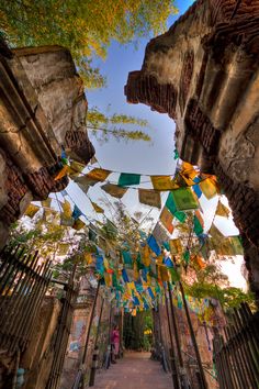 an alley way with colorful flags hanging from it's sides and trees in the background