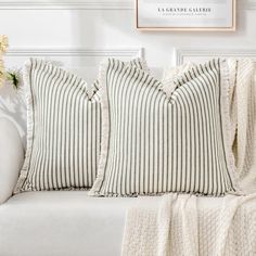 three pillows sitting on top of a white couch next to a vase filled with flowers