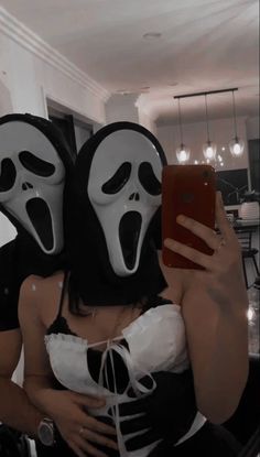 two people with masks on taking a selfie in front of a mirror while holding a cell phone