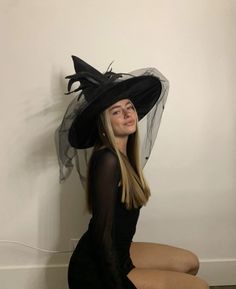 a woman sitting on the floor wearing a black hat with veil and hair in it