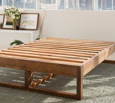 a wooden bed frame sitting on top of a carpeted floor next to a window