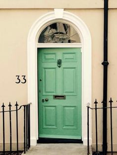 a green door with a white arch and black iron fence around it, in front of a house