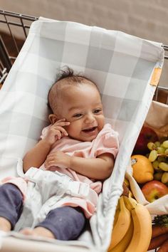 a baby sitting in a shopping cart with bananas and other fruits behind it, smiling