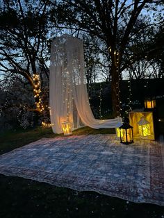 an outdoor area is lit up at night with lights and curtains on the ground, surrounded by trees