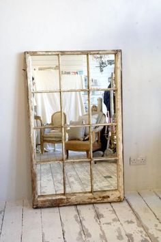 an old mirror is sitting on the floor in front of a white wall and chair