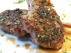 two pieces of meat sitting on top of a white plate covered in sauce and herbs