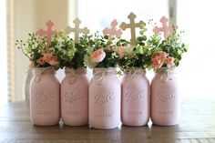 four pink mason jars with flowers and crosses on them are sitting on a wooden table