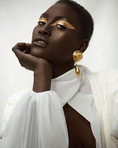 a woman with gold makeup on her face and neck, posing for a photo in white dress