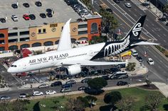 an air new zealand jetliner flying over a parking lot with cars and buildings in the background