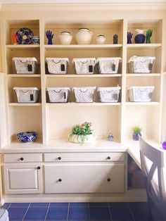 a white shelf filled with baskets and bowls on top of it's sides next to a table