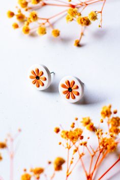 two small white and orange flower studs sitting on top of some yellow flowers next to each other