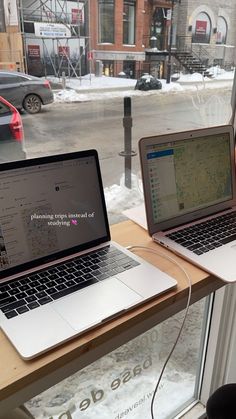 two laptops are sitting on a window sill in front of a snowy street