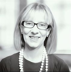 black and white photo of a woman with glasses smiling at the camera while wearing a beaded necklace