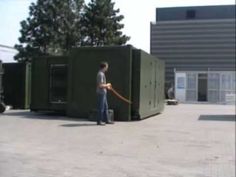 a man with a hose is standing in front of some green portable toilets and looking at the ground