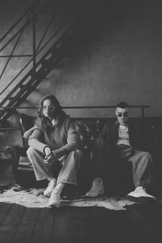 black and white photograph of two people sitting on a couch in front of a stair case