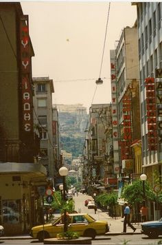 a busy city street with cars and people walking on the side walk in front of tall buildings