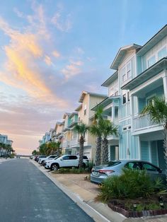 several cars parked on the side of an empty street in front of apartment buildings at sunset