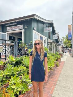 a woman standing in front of a building with lots of plants on the side walk