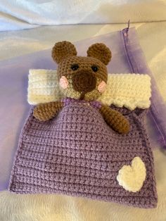 a crocheted teddy bear laying on top of a purple and white blanket next to a bag