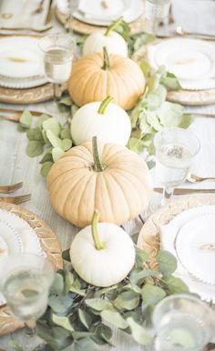 the table is set with white pumpkins and greenery