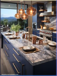 a kitchen with marble counter tops and blue cabinets, hanging lights over the island area