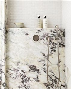 a bathroom with marbled walls and flooring, including a shower head in the corner