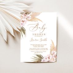 a white and pink floral baby shower card with palm leaves on it next to a plant