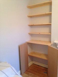 an empty room with some shelves in the corner and a bed on the other side