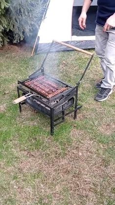 a man standing next to a grill on top of grass