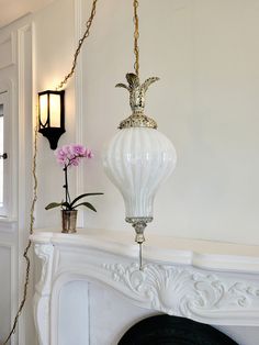 a white fireplace with a lamp hanging from it's side next to a potted plant