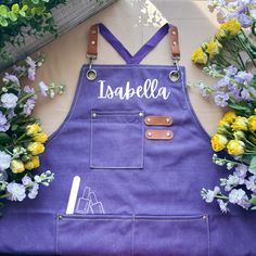 a purple apron with the name usaella written on it and flowers surrounding it in front of a fence