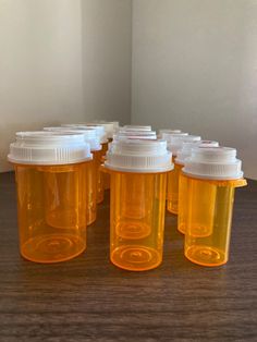 six orange plastic bottles with white caps are lined up on a wooden table in front of a wall