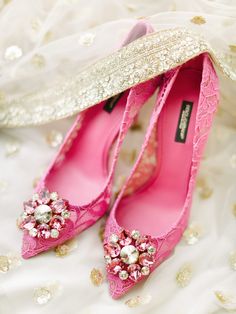 a pair of pink high heel shoes sitting on top of a white bed covered in gold sequins