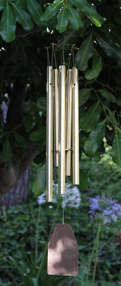 a wind chime hanging from a tree in front of some bushes and trees with purple flowers